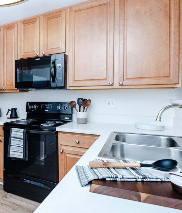 IMT Stevenson Ranch - modern kitchen with black appliances and white sleek countertops decorated with dark wood cutting board and wooden spoon