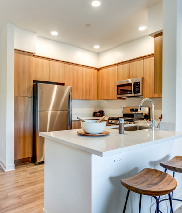 modern apartment kitchen with white countertops and wood cabinets with matching wood barstools