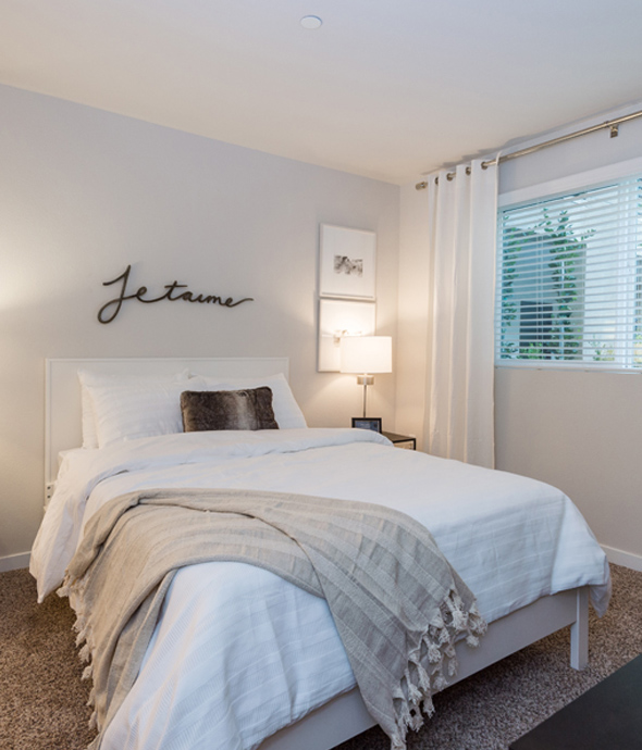 apartment bedroom with ceiling to floor white curtains and a white plush bedding
