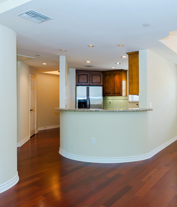 spacious apartment with dark wood floors a circular counter that curves into the kitchen with a beige marbled counter top