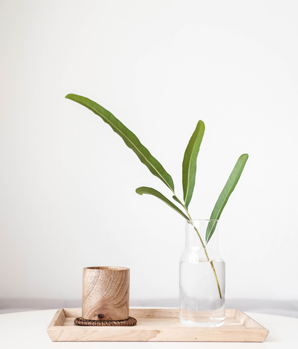 wood serving try on white table in the tray a long stem plant sits in vase and next to it a wooden cup