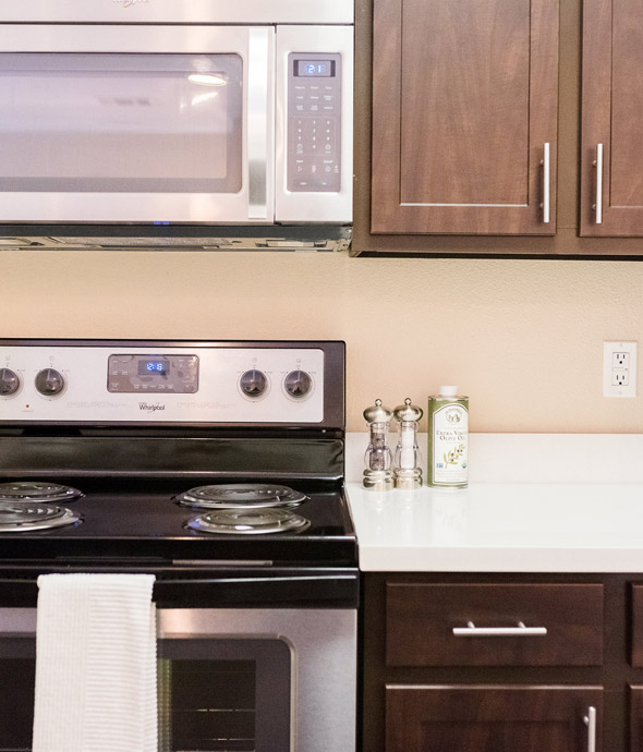 detail of apartment kitchen with updated black appliances cherry wood cabinets and white modern countertops