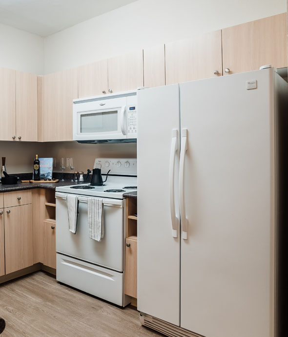 modern kitchen featuring white appliances with sand wood cabinets with a deep grey granite countertop