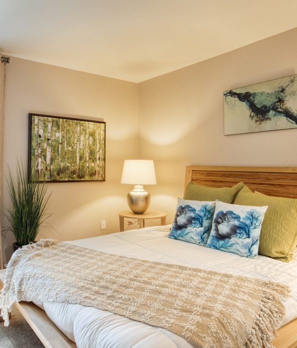 apartment bedroom in warm lighting with a modern wood bed frame and quilted comfortable bedding