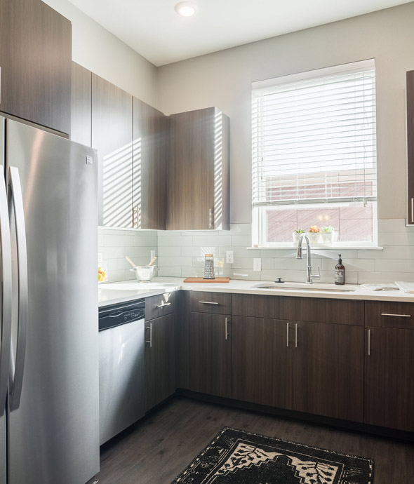 sun light shining through a kitchen window featuring stainless steel appliances, white counters and thick rich wood cabinets