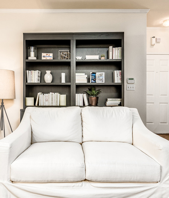 apartment room with white luxury couch, dark wood bookshelf behind couch