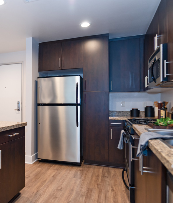 apartment kitchen with updated stainless steel appliances, granite countertops and dark wood cabinets