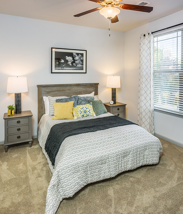 IMT Ballantyne - Bedroom with plush carpet, platform bed with comfortable bedding, wood bedside tables with lamps, and large window.