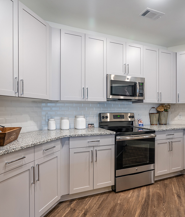 Kitchen with smooth countertops, white cabinets, rich wood floor, and stainless steel appliances.