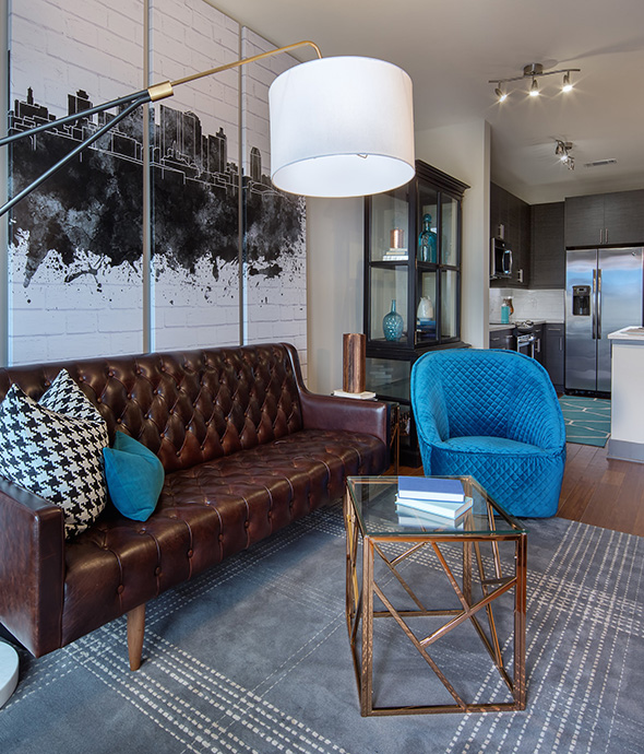 Apartment living room with rich leather couch, standing lamp with cylinder shade, and skyline wall graphic.