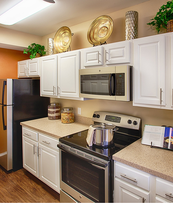 Kitchen with wood floors, white cabinets, stainless steel appliances, and orange accent wall.