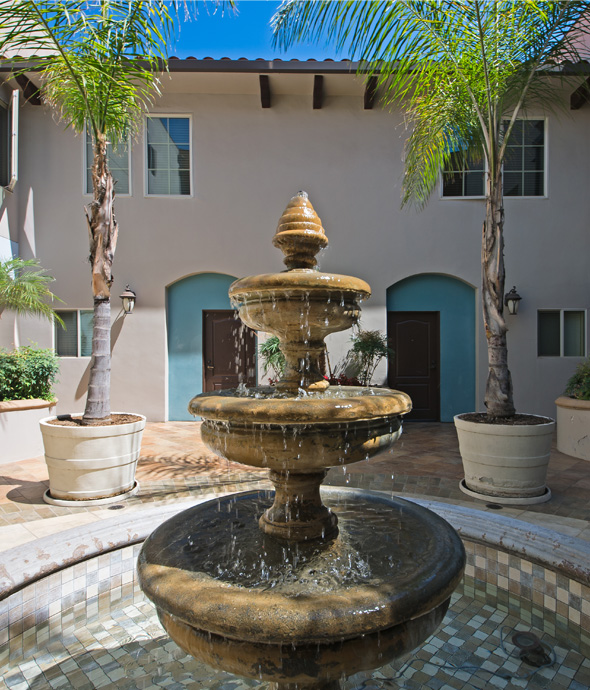 outdoor royal water fountain sitting in between two large potted flourishing palm trees
