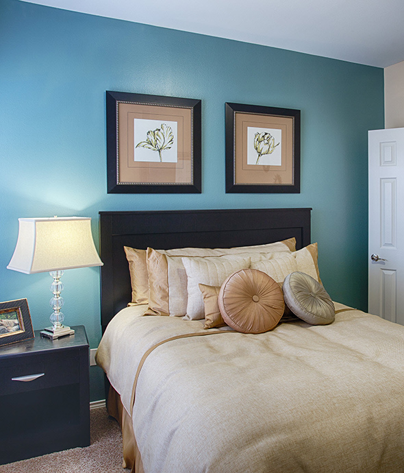 Bedroom with large bed, plush bedding, wood bedside table with lamp, and wall art.
