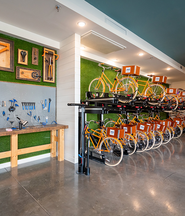 Bicycle repair room with bikes on racks, pegboard workbench with tools, and smooth concrete floors.