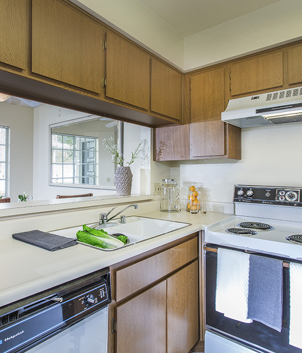 Kitchen with wood cabinets, light countertops, and white appliances and sink with washed vegetables.