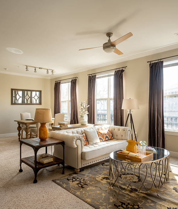 Living room with rug, plush couch, metal side tables, and large windows with curtains.