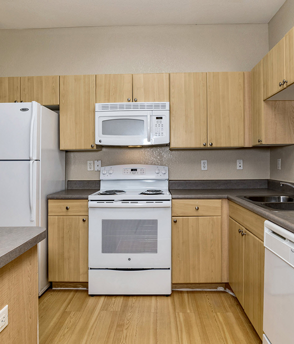 Kitchen with white appliances, light wood cabinetry, grey countertops, hardwood flooring, and island.