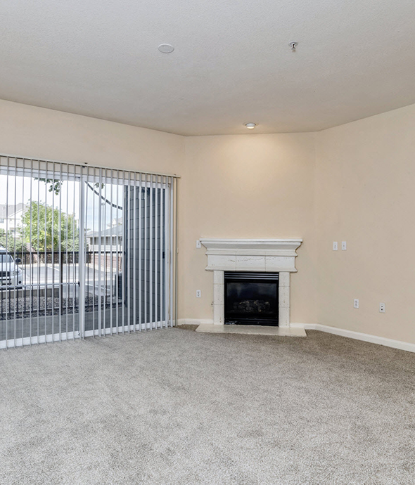 Open living room with carpet flooring, ceiling fan, fireplace and mantel, and sliding glass door leading out to patio.