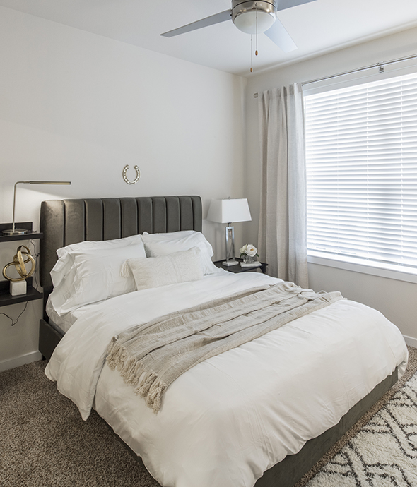 Bedroom with carpet, platform bed with plush bedding, shelves with decor, and large window.