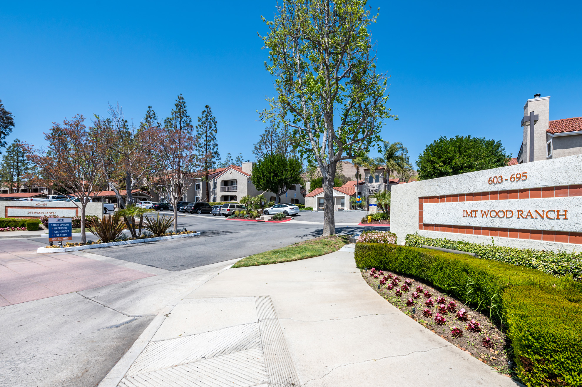 IMT Wood Ranch - Sign in front of the exterior of the building with paved walkway, greenery, and street