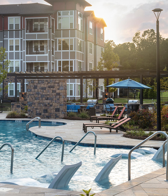 Pool area with in pool lounge chairs, stone paver patio, lounge chairs, and stone fireplace.