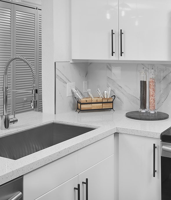 Kitchen with white cabinets and counters, stainless steel sink, and large salt and pepper mills.