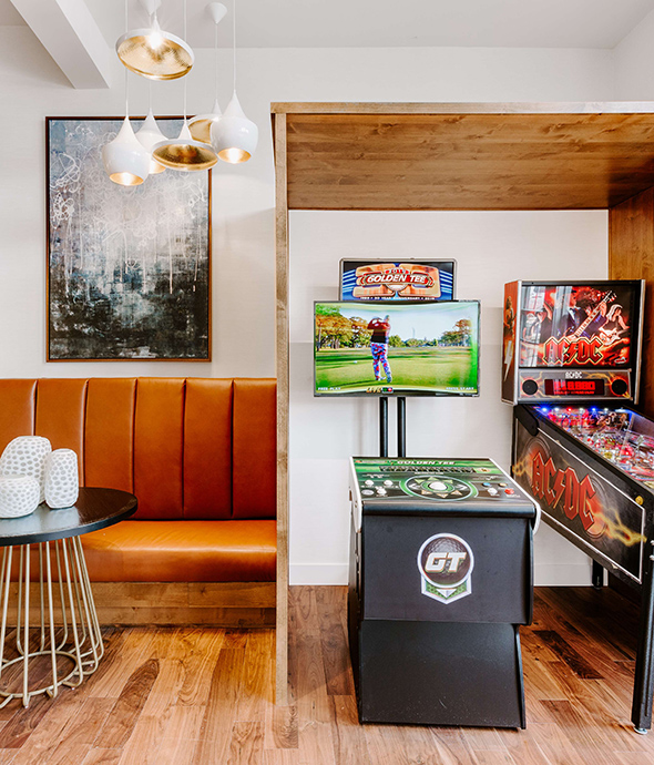 IMT Lowry - Game area with golden tee and pinball games, wood floor, and modern light fixture.