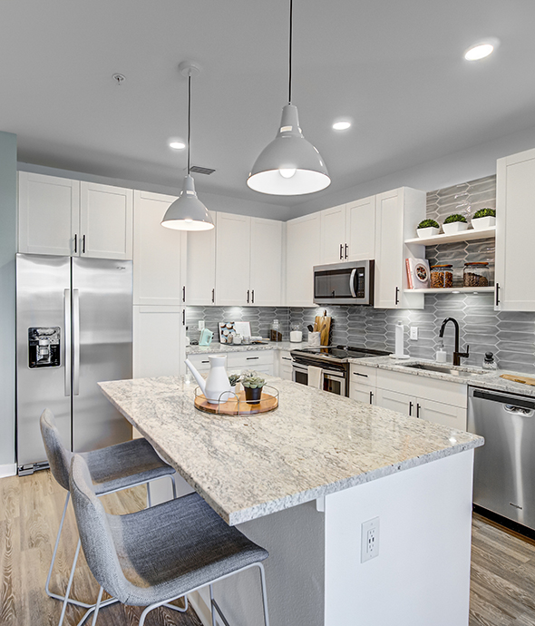 IMT Lakehouse - Kitchen with wood floor, white cabinets, stone counters, and stainless steel appliances.