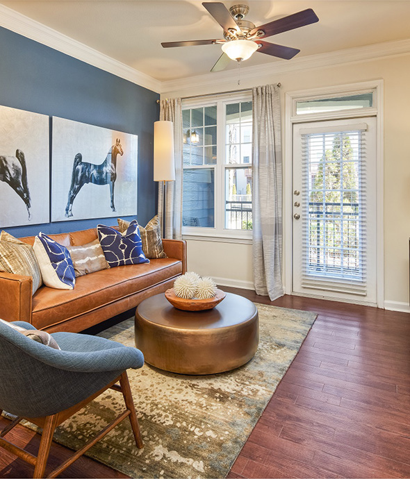 Living room with wood floor, plush rug, leather couch, eclectic decor, and door to balcony.