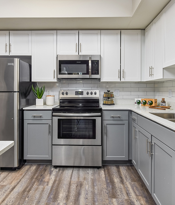 Kitchen with wood floor, two tone cabinets, stone counters, and stainless steel appliances.