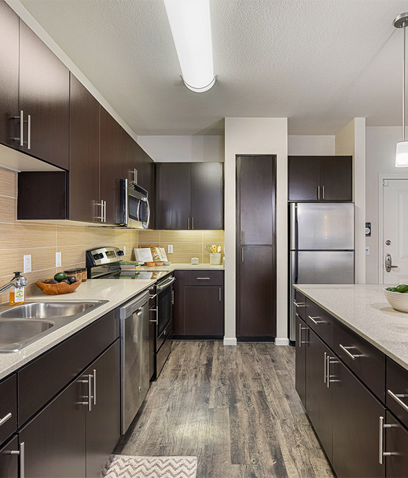 Apartment kitchen with wood style floor, wood cabinets, and stainless steel appliances.